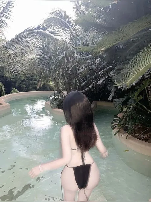 Thiếu nữ bikini trắng ngồi trên thảm ngoài trời, nón rộng vành che kín mặt trong tư thế thư giãn.