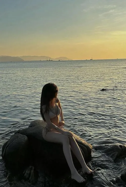 Mỹ nhân bikini đỏ nằm dài trên cát biển lúc hoàng hôn, tay đưa lên che mắt.