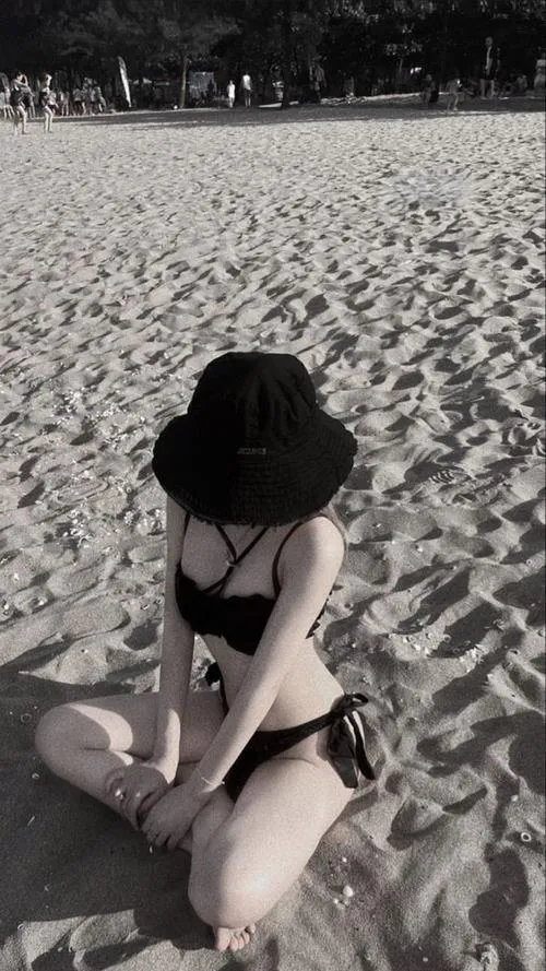 Cô nàng trong bikini đen ngồi co chân trên cát mịn, mái tóc dài xõa xuống giấu kín mặt trong lúc ngắm biển xanh.