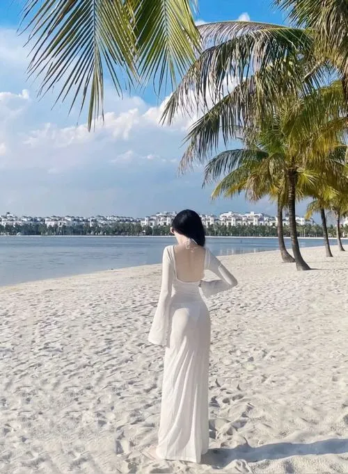 Cô nàng mặc váy trắng bước chậm trên bãi cát rợp bóng dừa, lưng quay về máy ảnh và dáng đi thong thả gợi một vẻ đẹp tự nhiên rất dễ chịu