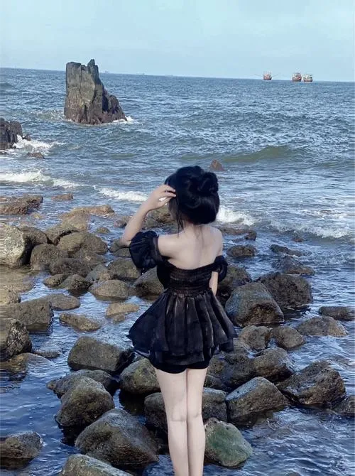 Bộ váy đen xòe ngắn ôm theo gió khi cô đứng giữa bãi đá ven sóng, góc chụp sau lưng khiến người đẹp áo tắm chụp từ phía sau càng thêm cuốn