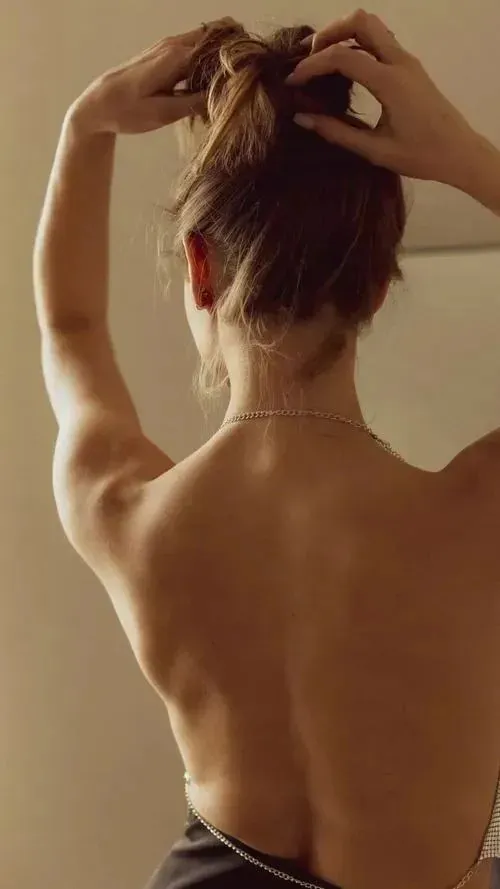 Nàng nằm nghiêng co chân, một tay nâng cằm và đường cong lưng uyển chuyển dưới ánh đèn studio.