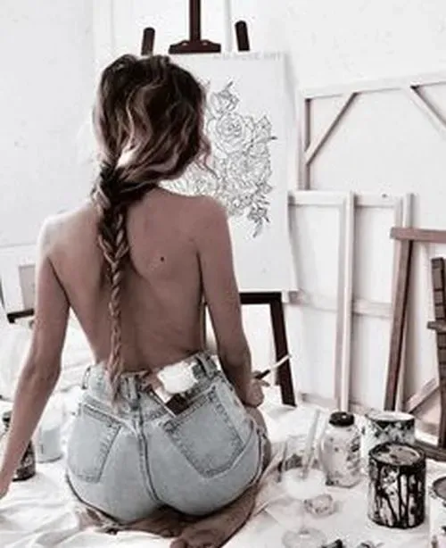 Nàng quay lưng hoàn toàn với tay ôm tóc, tấm lưng trần và hông cong nhẹ trong ánh sáng dịu.