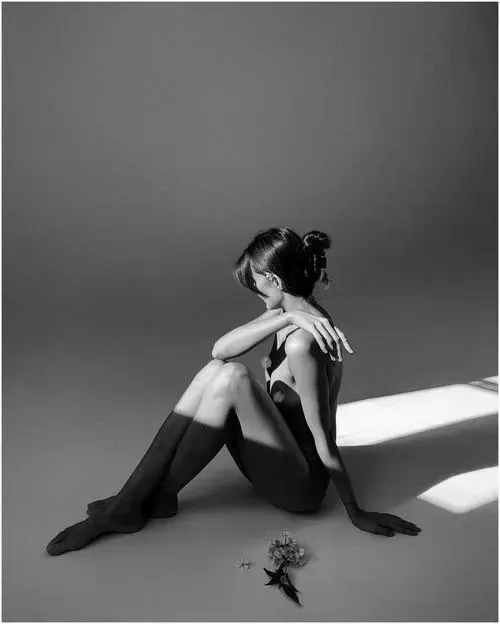 Gái đẹp ngồi co chân trên thảm, cằm tựa đầu gối nhìn ra xa với biểu cảm bình yên dưới ánh sáng tự nhiên.