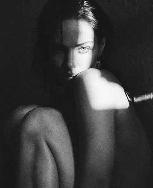 Nàng đứng thẳng buông tay dọc thân, gương mặt ngẩng nhẹ với nụ cười kín đáo giữa nền tối giản trắng.