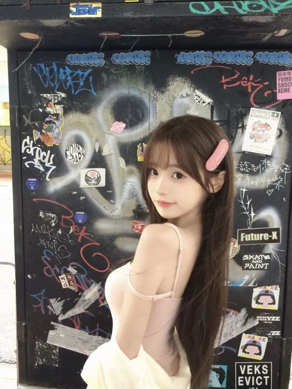 Bóng hồng ngồi trước bức tường vẽ phấn, váy trắng ôm nhẹ và mái tóc nâu dài khiến dáng ngồi nghiêng của cô trông nhã nhặn mà cuốn mắt