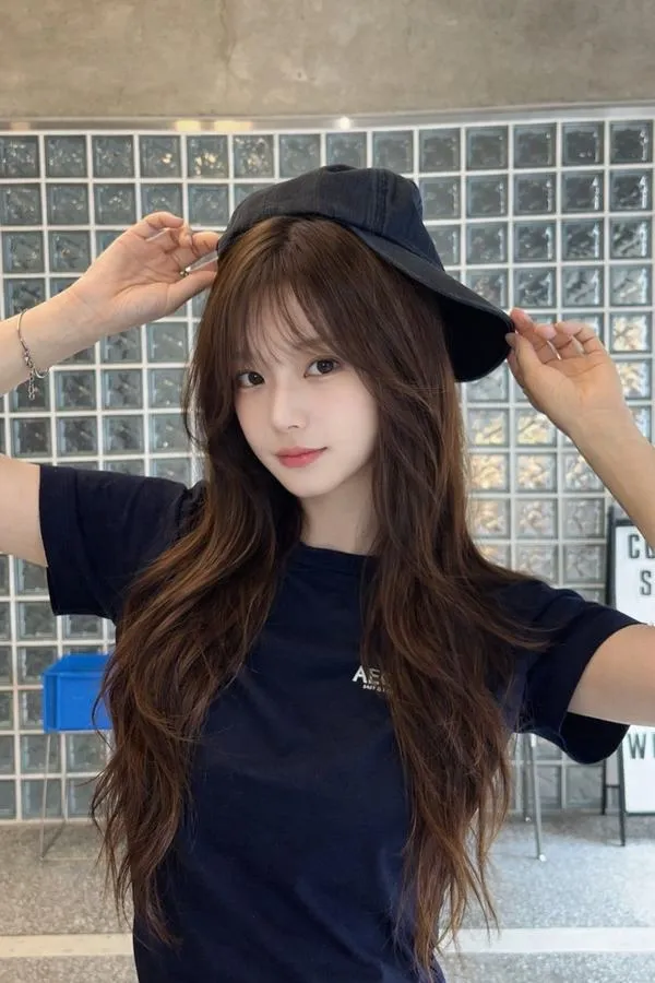 Hot girl tỷ dân đội mũ đen trước bức tường kính gạch, áo xanh đậm ôm gọn thân trên và nụ cười nhẹ tạo cảm giác năng động ngoài biển