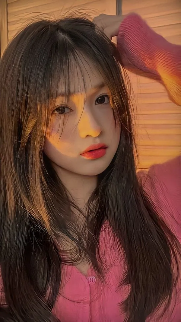 Khung dọc bắt trọn cô gái tóc nâu sẫm đứng trong phòng ánh vàng, môi cam nổi bật trên áo hồng hai dây tạo cảm giác vừa cá tính vừa gọn gàng