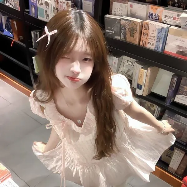 Trong góc quán sách, cô nàng áo ren trắng cúi đầu mỉm cười, mái tóc nâu dài và ánh đèn vàng khiến cả khung hình trông ngọt lành