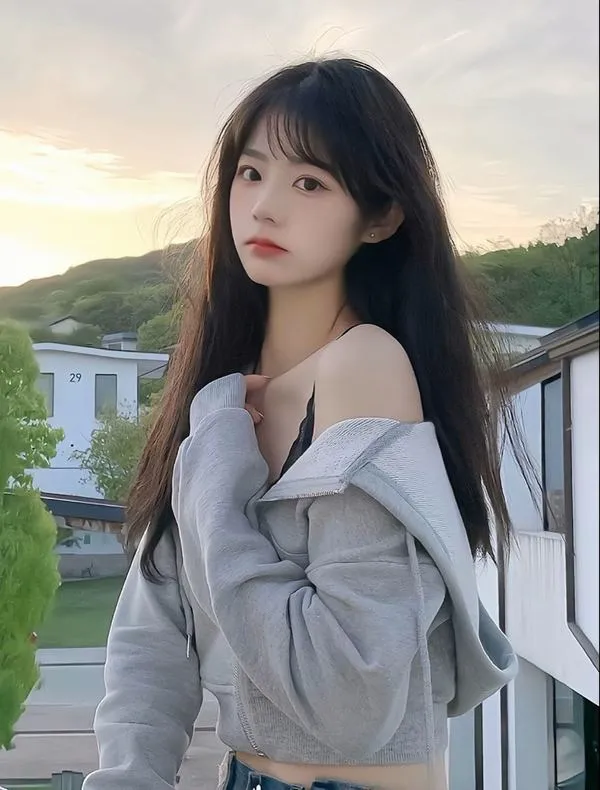 Gái đẹp xứ Trung đứng bên lan can với áo khoác ghi trễ vai, tóc đen dài và ánh mắt hướng xa làm nền đồi sau lưng thêm thoáng đãng