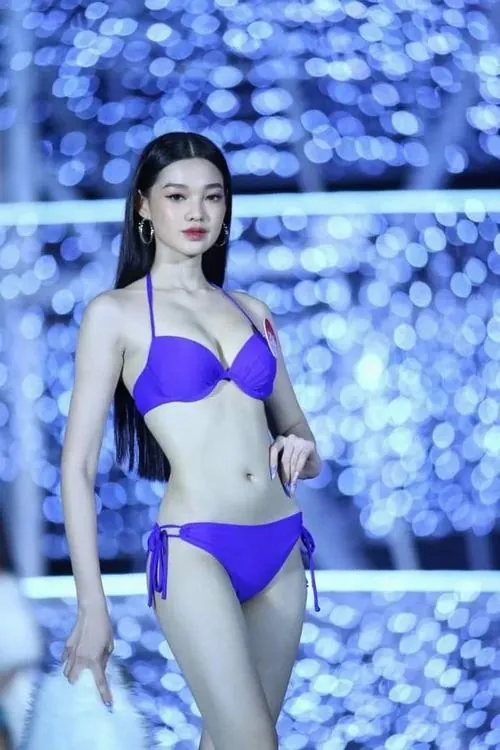 Góc ảnh cận toàn thân của cô gái mặc bikini tím trên sân khấu xanh, mái tóc đen dài và tư thế một chân bước lên tạo vẻ sắc sảo