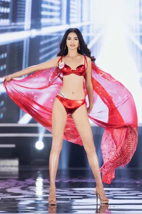 Khung dọc bắt trọn cô gái đứng giữa sân khấu với bikini đỏ và lớp voan hồng, dáng thẳng người cùng nụ cười nhẹ nhìn khá bắt mắt