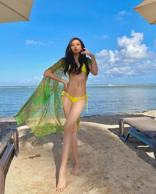 Góc chụp bắt người mẫu đứng trên cát với khăn voan xanh mỏng phủ tay, bikini nhỏ và gió biển thổi tà khăn tạo cảm giác rất bay bổng