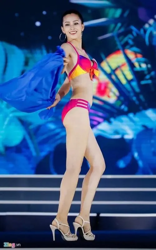 Ảnh dọc ghi lại cô gái catwalk trong bikini nhiều màu dưới ánh đèn sân khấu, bước chân dài và thân người nghiêng làm tổng thể rất sôi động