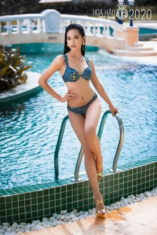 Hình chụp người mẫu đứng thẳng ở mép nước, bikini xanh ngọc nổi bật dưới nắng, đôi chân dài và vẻ mặt tự tin làm đường cong chữ S hiện rõ