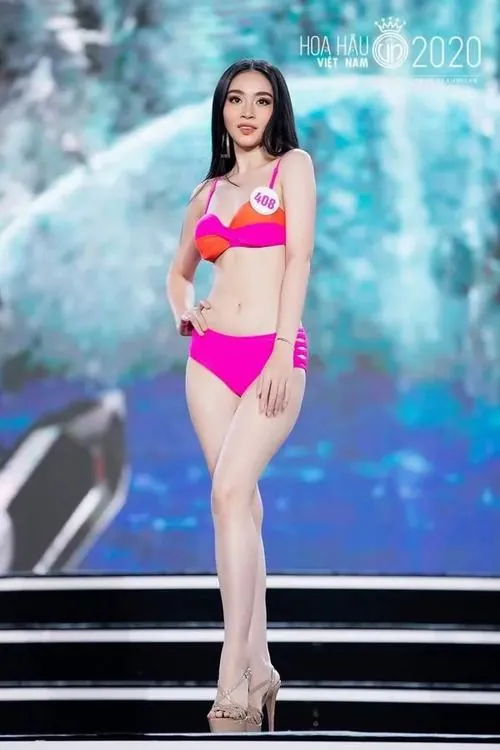 Khoảnh hình ghi người mẫu bước trên sân khấu với bikini hồng, nền xanh mờ phía sau và dáng catwalk gọn gàng tạo cảm giác rất tươi mới