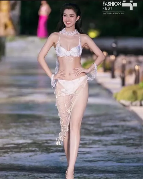 Ảnh chụp người mẫu bước trên mặt nước nông với váy lưới trắng ôm người, tóc búi cao và nụ cười nhẹ khiến dáng vẻ rất thanh thoát