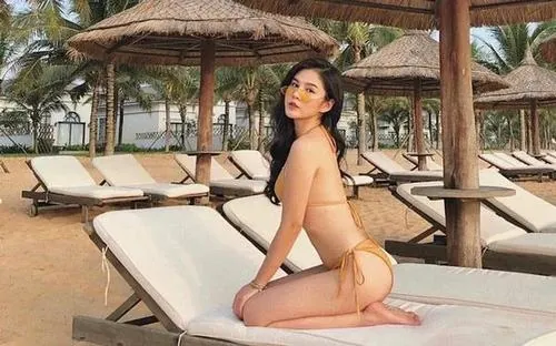 Hình nền ghi cô gái ngồi nghiêng trên ghế nghỉ dưới mái chòi, bikini màu be và tư thế chống tay làm khung cảnh resort trông thật thư thái