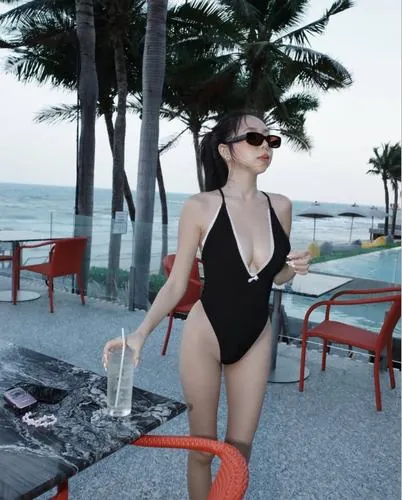 Cô nàng ngồi trên ghế gỗ gần hồ, diện áo tắm một mảnh màu đen, chân co nhẹ, ánh mắt nhìn xuống tạo cảm giác dịu dàng