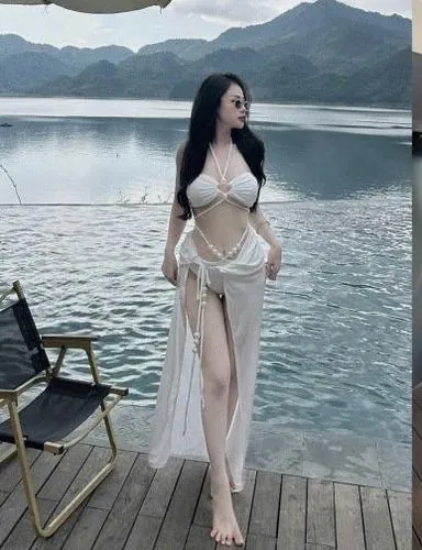 Cô gái ngồi bên thành hồ, tay chống phía sau, bikini trắng kết hợp ánh nước xanh tạo cảm giác mát và thoáng
