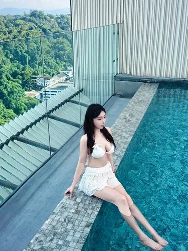 Ảnh bìa người mẫu đứng quay lưng dưới hàng cọ, tay chạm tóc, set đồ bơi trắng thanh khiết tạo điểm nhấn rõ ràng trên nền cây xanh và nắng gắt