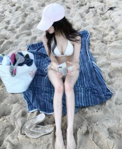 Cô nàng đứng bên khăn trải màu xanh, tay cầm túi nhỏ, đồ bơi trắng tinh kết hợp phụ kiện đơn giản tạo tổng thể nhẹ nhàng và dễ nhìn