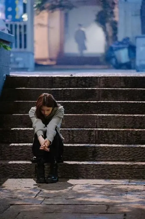 Người mẫu ngồi gục ở bậc thềm ngoài phố, hai khuỷu tay tì lên gối và ánh đèn mờ sau lưng khiến hình cô đơn này rất thật