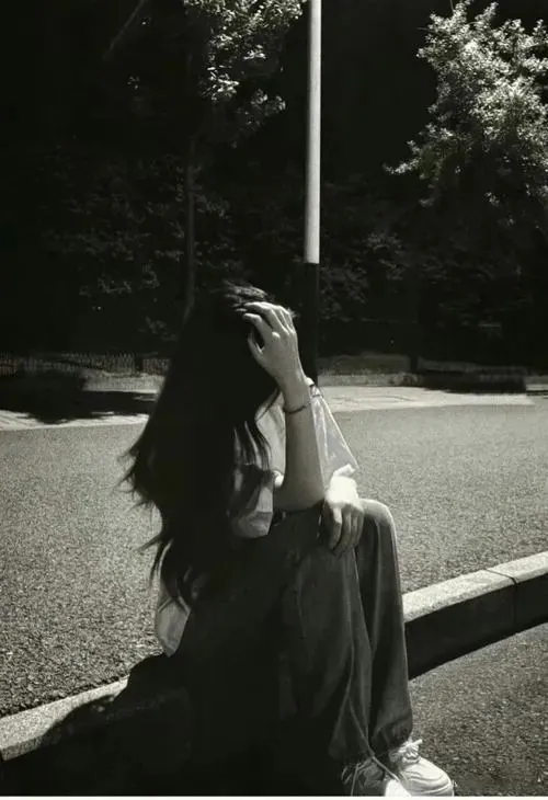 Hình nền ảnh profile cô gái tóc dài ngồi bên lề đường trắng đen, một tay chạm lên mái tóc và ánh nắng gắt làm dáng người khá mong manh