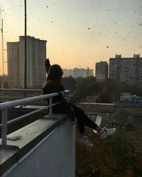 Cô nàng tựa người trên ban công cao tầng lúc hoàng hôn, áo tối ôm dáng và đường chân trời nhạt nắng khiến khung hình rất chênh chao