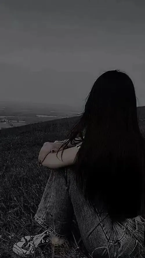 Cô gái tóc dài ngồi bó gối trên triền đất tối, lưng cúi hẳn xuống và nền đen mờ khiến dáng người trông tê tái giữa khoảng trống