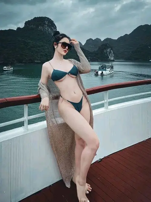 Tựa lưng vào tường, cô gái nằm nghiêng trong bộ đồ bơi xanh lá, một tay đưa lên đầu khiến dáng chân và eo hiện ra khá gọn mắt