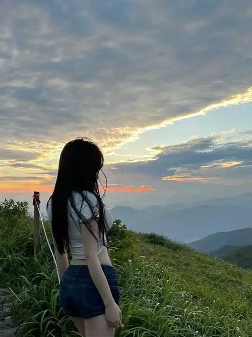 Cô nàng khoác áo măng tô mỏng đi qua dãy tủ đồ của trường học lúc chiều muộn tóc dài lướt trên lưng tạo nét mềm rất tự nhiên