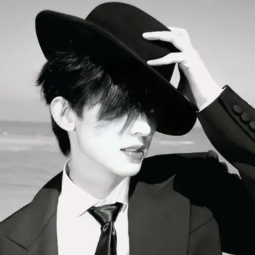 Hình profile người con trai mặc vest cùng mũ đen, tay nâng vành mũ khi cười nhẹ, nền sáng làm khung hình đẹp và hợp phong cách Minimalism