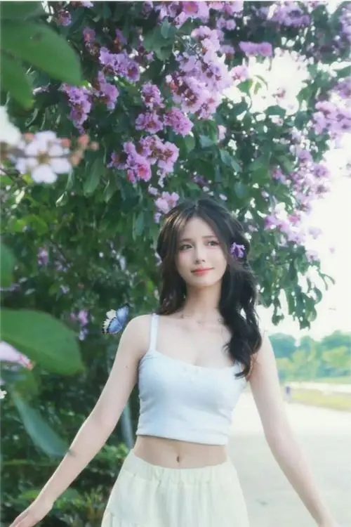 Cô đang quay người nhẹ nhìn qua vai bên bờ sông, váy trắng dài, tóc xõa bay trong gió, má hồng tự nhiên dịu dàng.