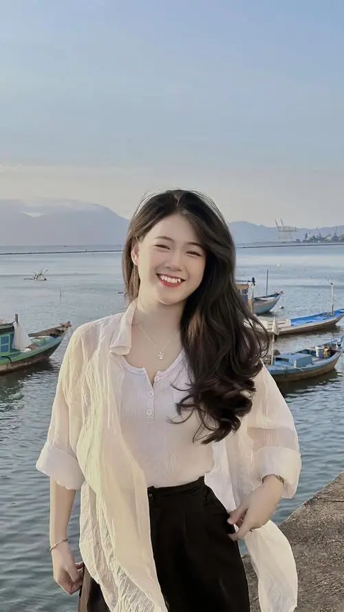 Nàng đang ngồi bên lan can ban công ngắm hoàng hôn, áo sơ mi oversize, tóc xõa vai, nụ cười nhẹ nhàng thanh thoát.