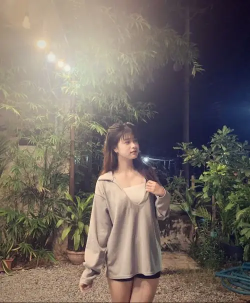 Thiếu nữ ngồi trên ghế đá công viên cầm cuốn sổ tay, váy dài pastel, tóc xõa nhẹ che má, mắt long lanh với nụ cười mỉm thanh tú.