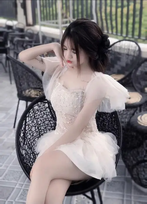 Nàng thơ đang nằm nghiêng trên thảm cỏ xanh mặc váy hoa nhí, tóc thả dài, mắt nhắm hờ mỉm cười dưới ánh nắng xuyên qua lá.