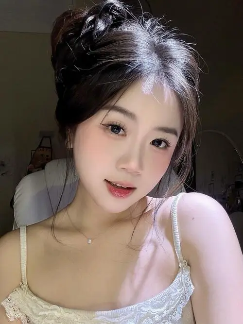 Ảnh gái đang cầm ly nước cam ngồi bên bàn ngoài trời, áo sơ mi trắng, tóc hai bên thả, nụ cười tươi tắn với má hồng tự nhiên.