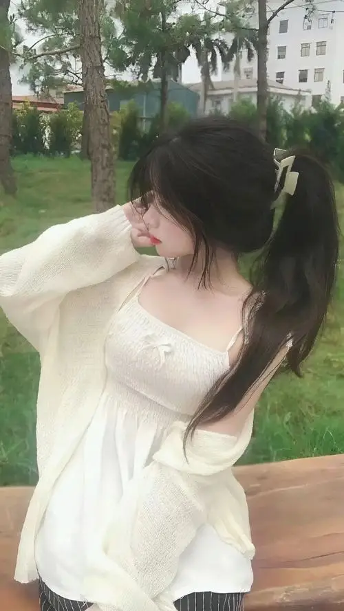 Em gái đang cúi xuống hái hoa dại mặc váy babydoll xanh nhạt, tóc hai bên thả lỏng, biểu cảm tập trung với má hồng tự nhiên rạng rỡ.