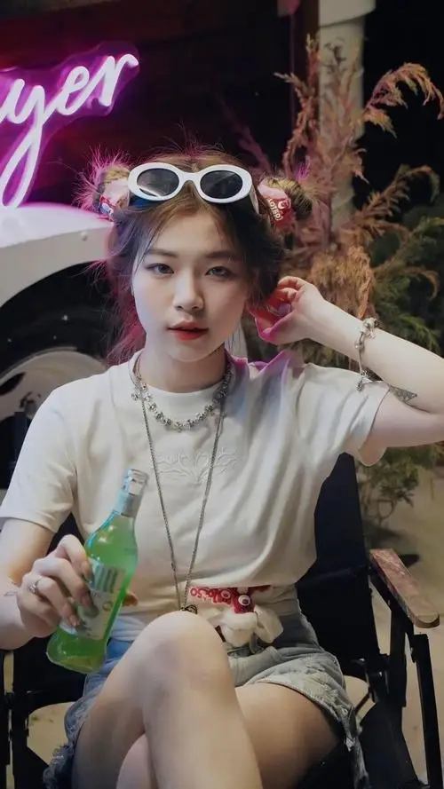 Cô đang đứng nghiêng người bên bức tường gạch cũ, tay cầm mũ nồi, tóc búi thấp, biểu cảm tinh nghịch với nụ cười hé môi duyên dáng.