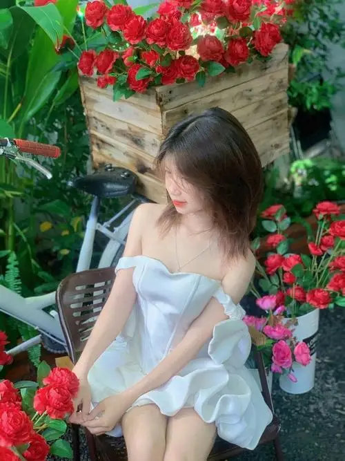 Gái xinh cúi nhẹ nhìn cuốn sách cũ trong lớp học đồng phục kẻ caro, tóc thắt hai bím nhỏ xinh, môi cong cong cười e thẹn dưới ánh đèn ấm áp.